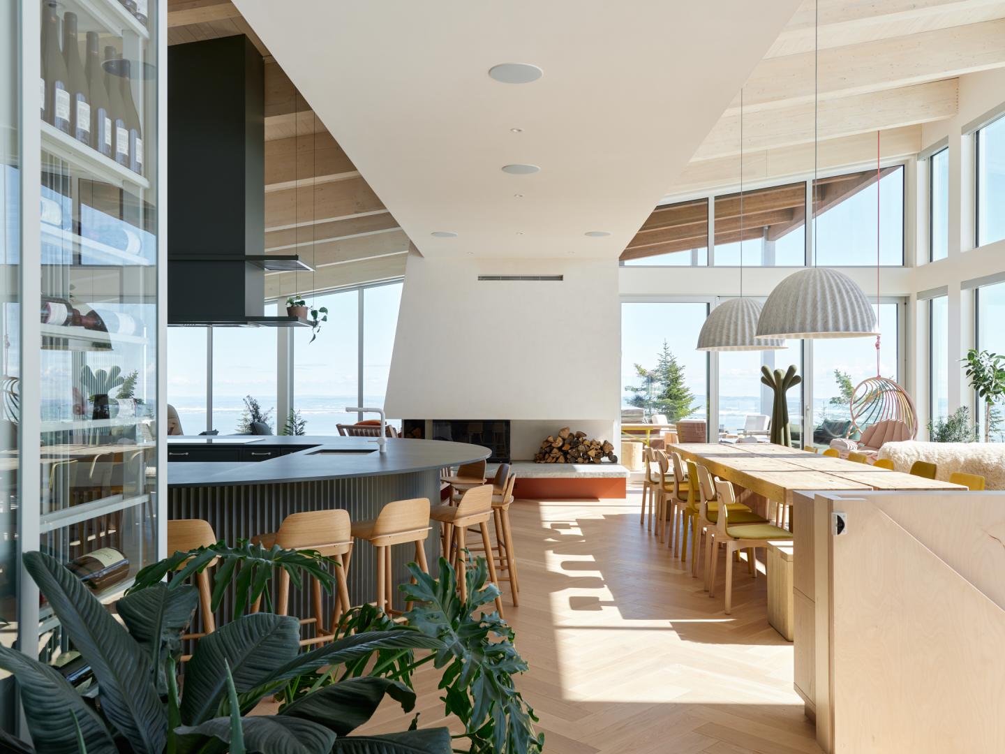 Intérieur lumineux avec table en bois, chaises, et grandes fenêtres donnant sur l'extérieur.