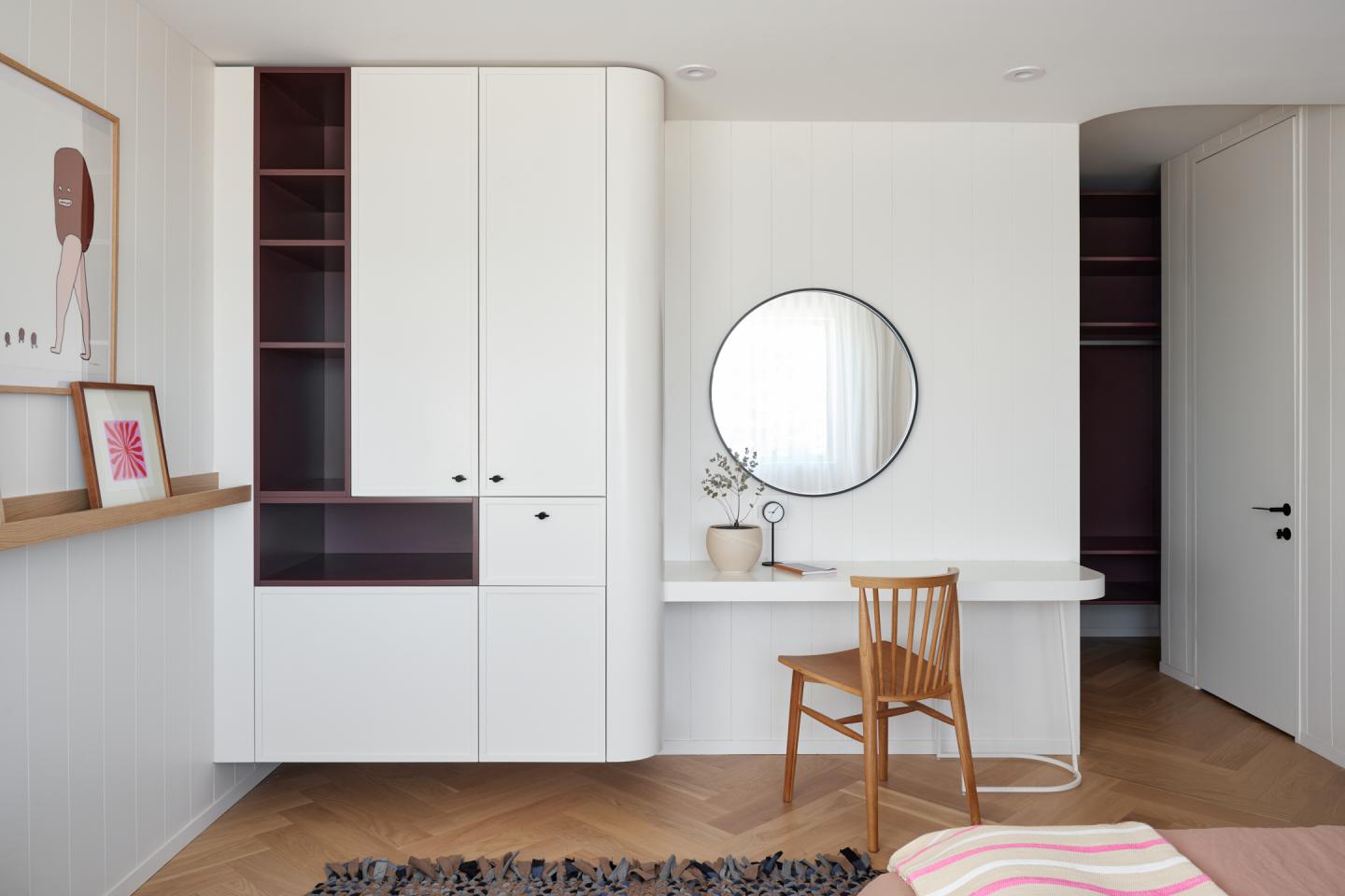 Chambre moderne avec bureau, miroir rond, chaise en bois, et placard blanc.