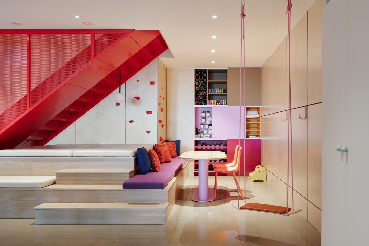 Salle de jeux moderne avec escalier rouge, sièges colorés et balançoire intérieure.