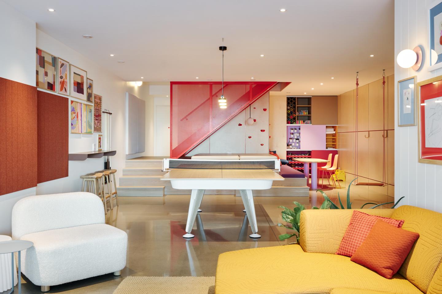 Salon moderne avec canapé jaune, table de billard blanche, et escalier rouge.