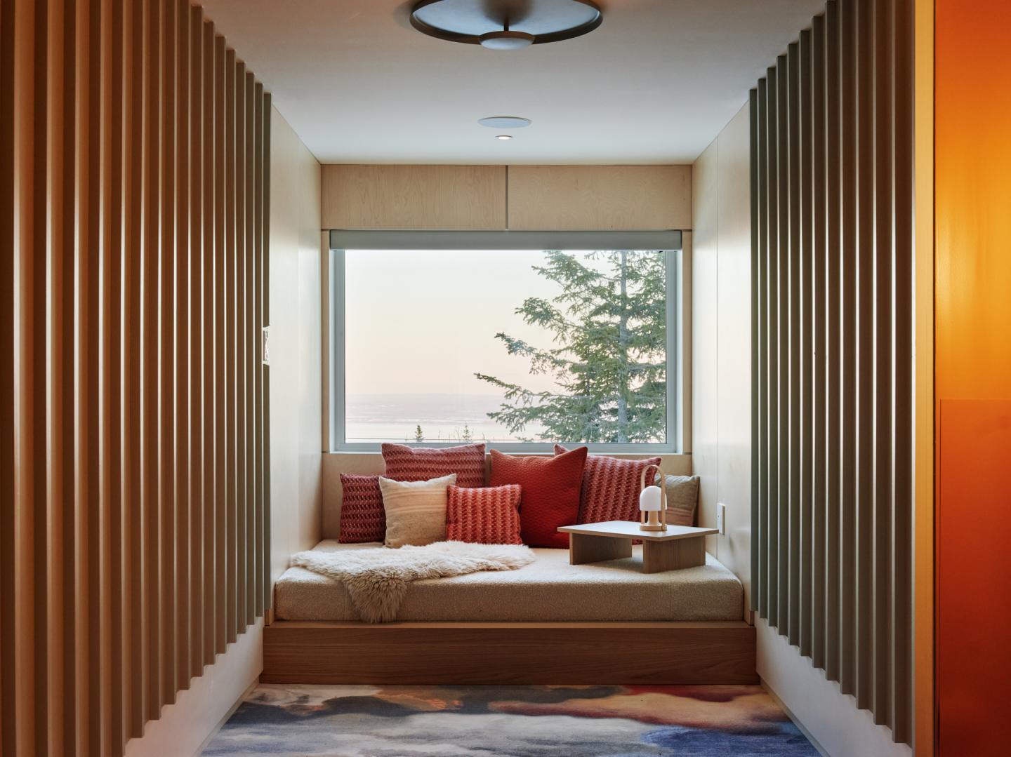 Fenêtre avec vue sur un arbre, coussins rouges sur canapé, ambiance chaleureuse.