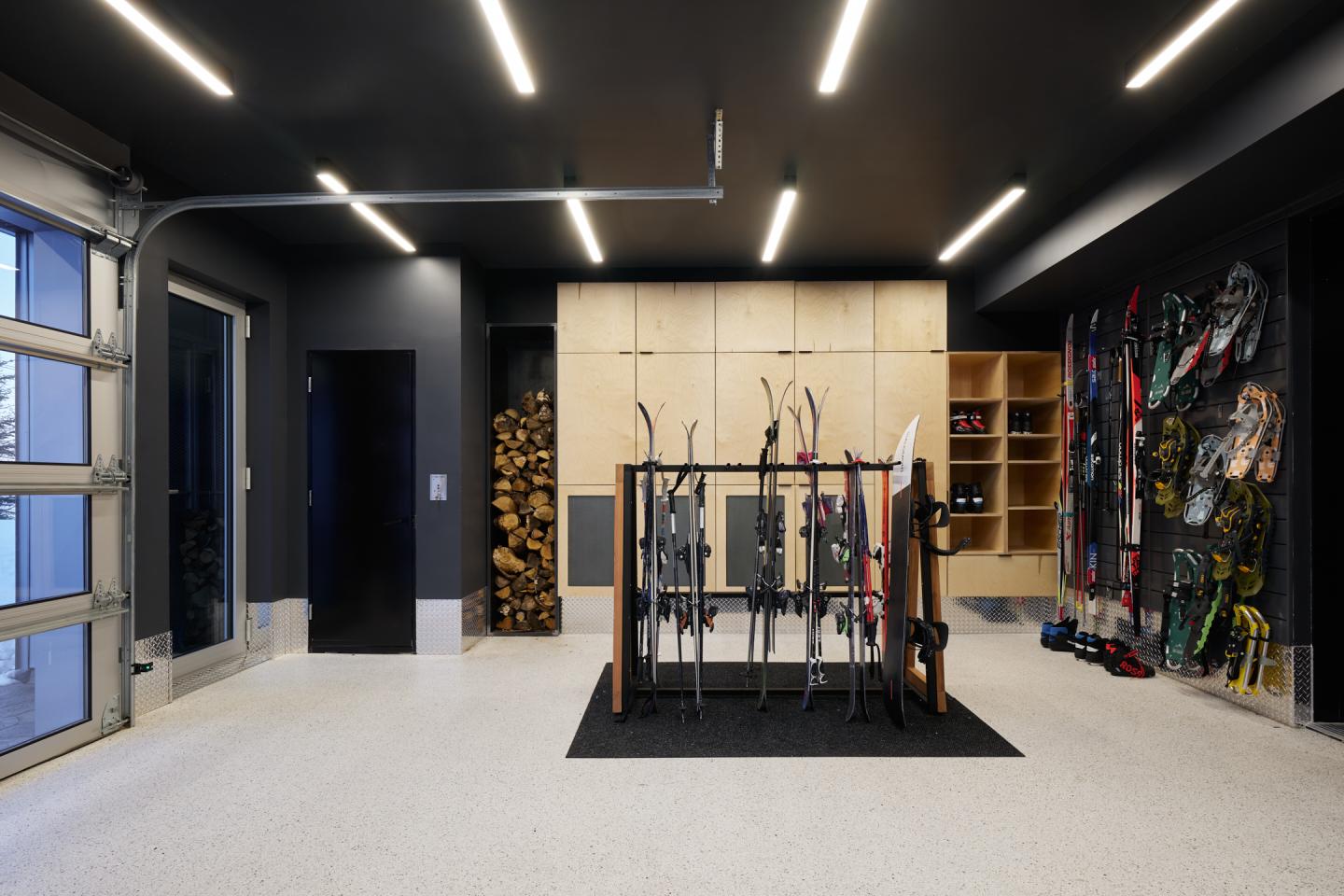 Garage moderne avec skis rangés sur un support, murs sombres et éclairage intégré.