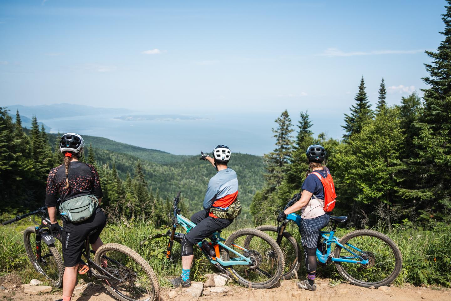 Trois cyclistes sur une sentier de vélo de montagne du Massif de Charlevoix, admirant le fleuve St-Laurent