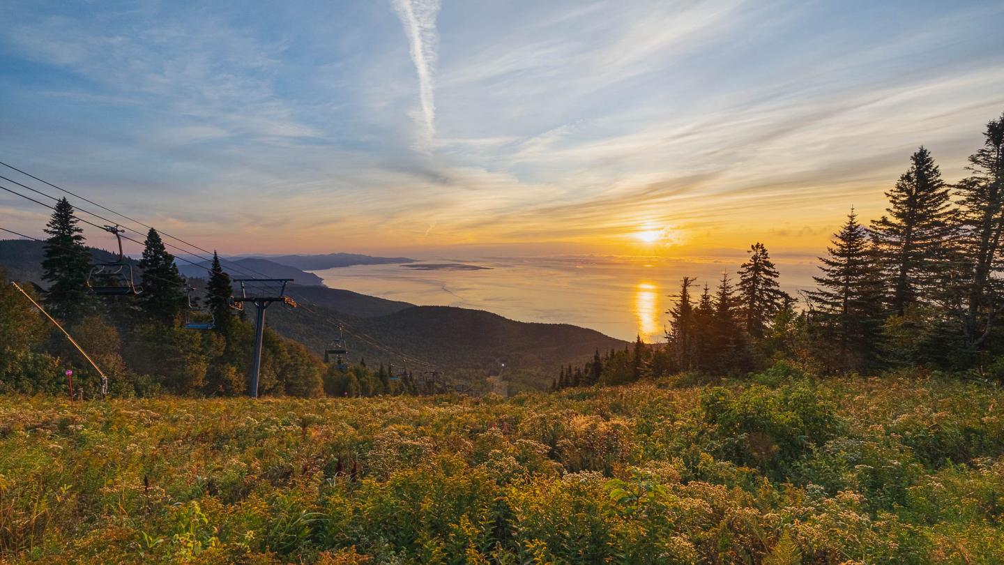 Coucher de soleil sur une vallée boisée avec un lac scintillant à l'horizon.