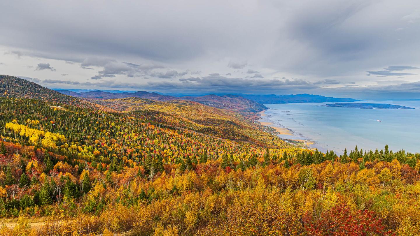 Paysage automnal coloré avec forêt, montagne et lac sous ciel nuageux.