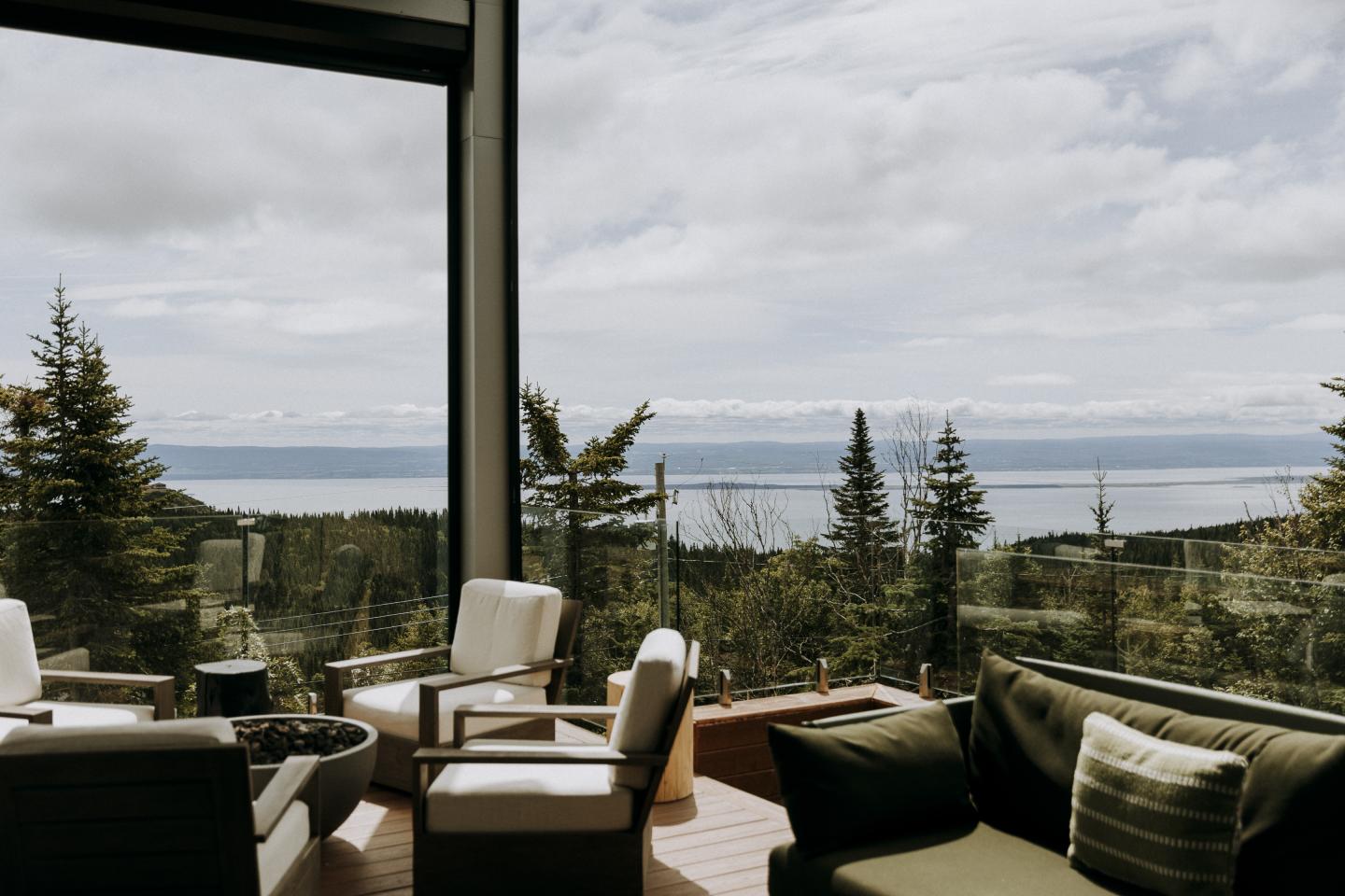 Terrasse avec sièges, vue sur forêt et mer sous ciel nuageux.
