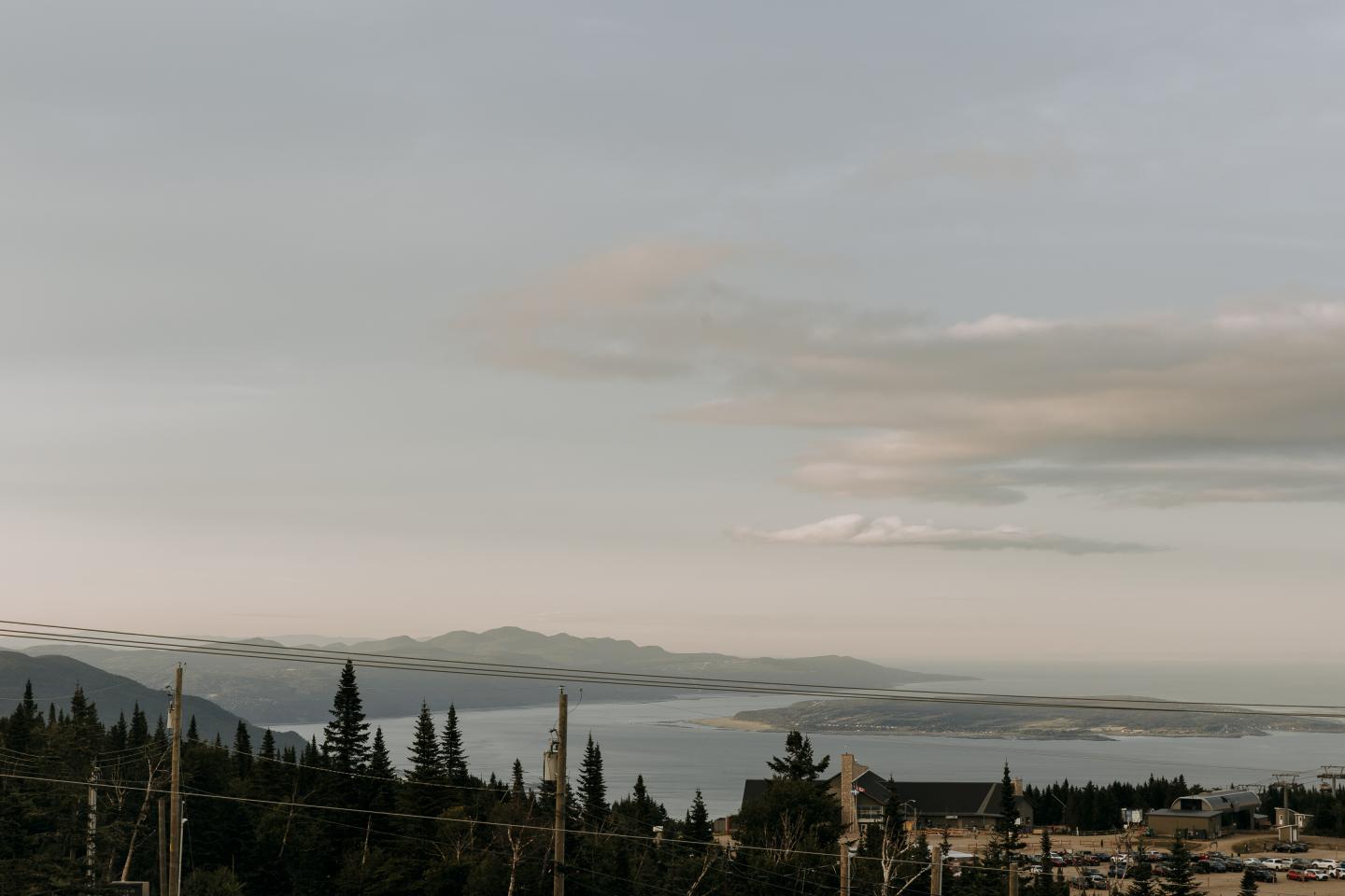 Vaste paysage montagneux sous un ciel nuageux, arbres et mer à l'horizon.