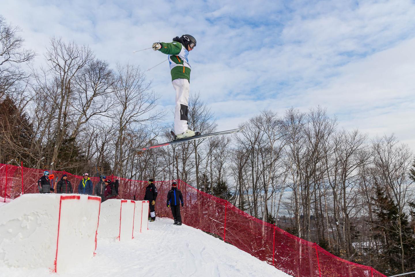 Skieur sautant en l'air sur une pente enneigée, ciel bleu en arrière-plan.