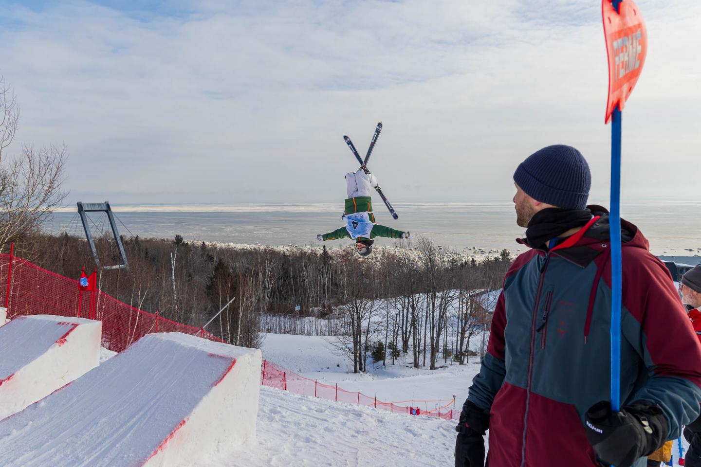Skieur en plein saut acrobatique, observé par une personne en tenue d'hiver.