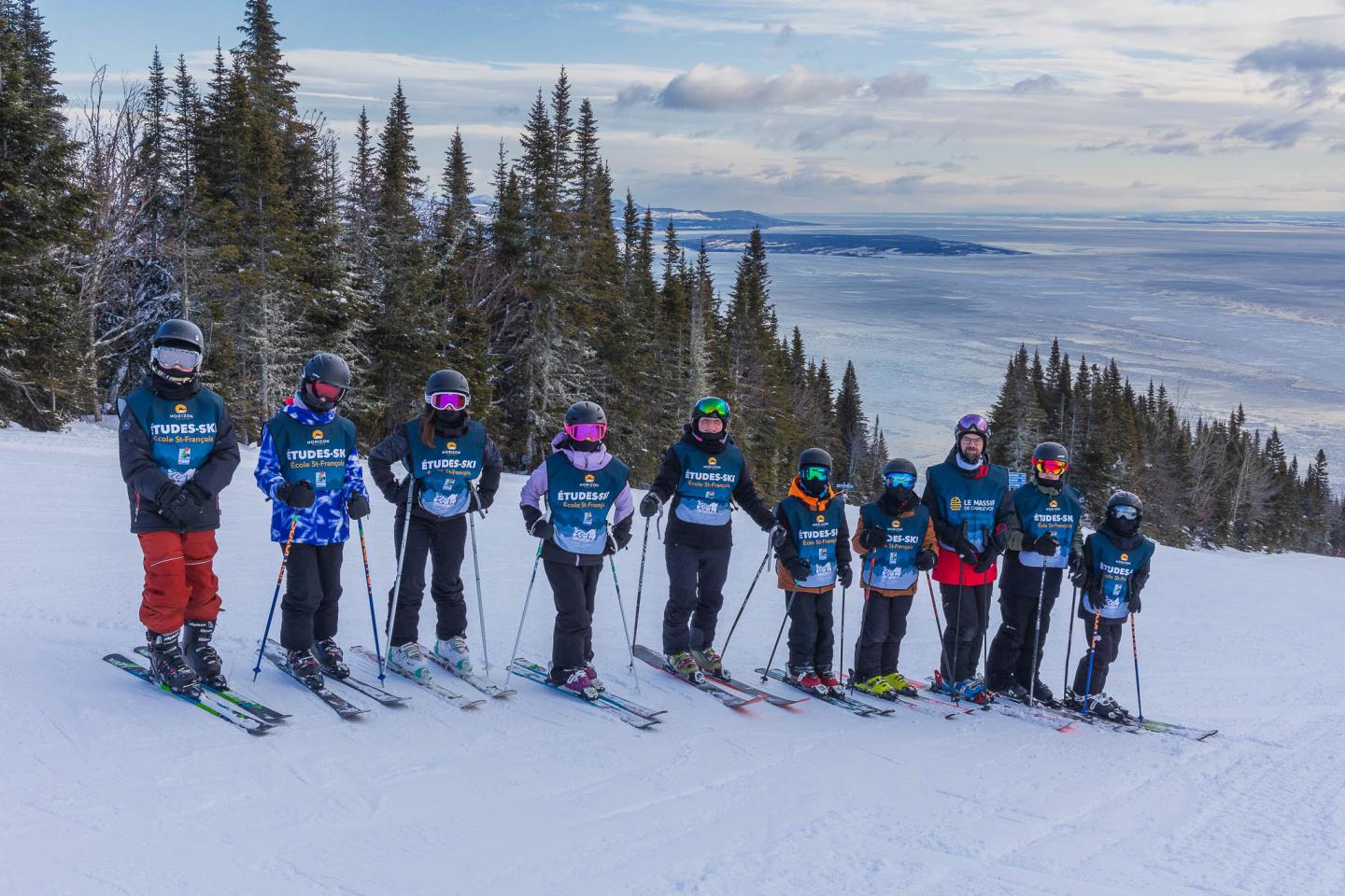 Onze personnes en ski alignées sur une piste enneigée, avec une forêt en arrière-plan.
