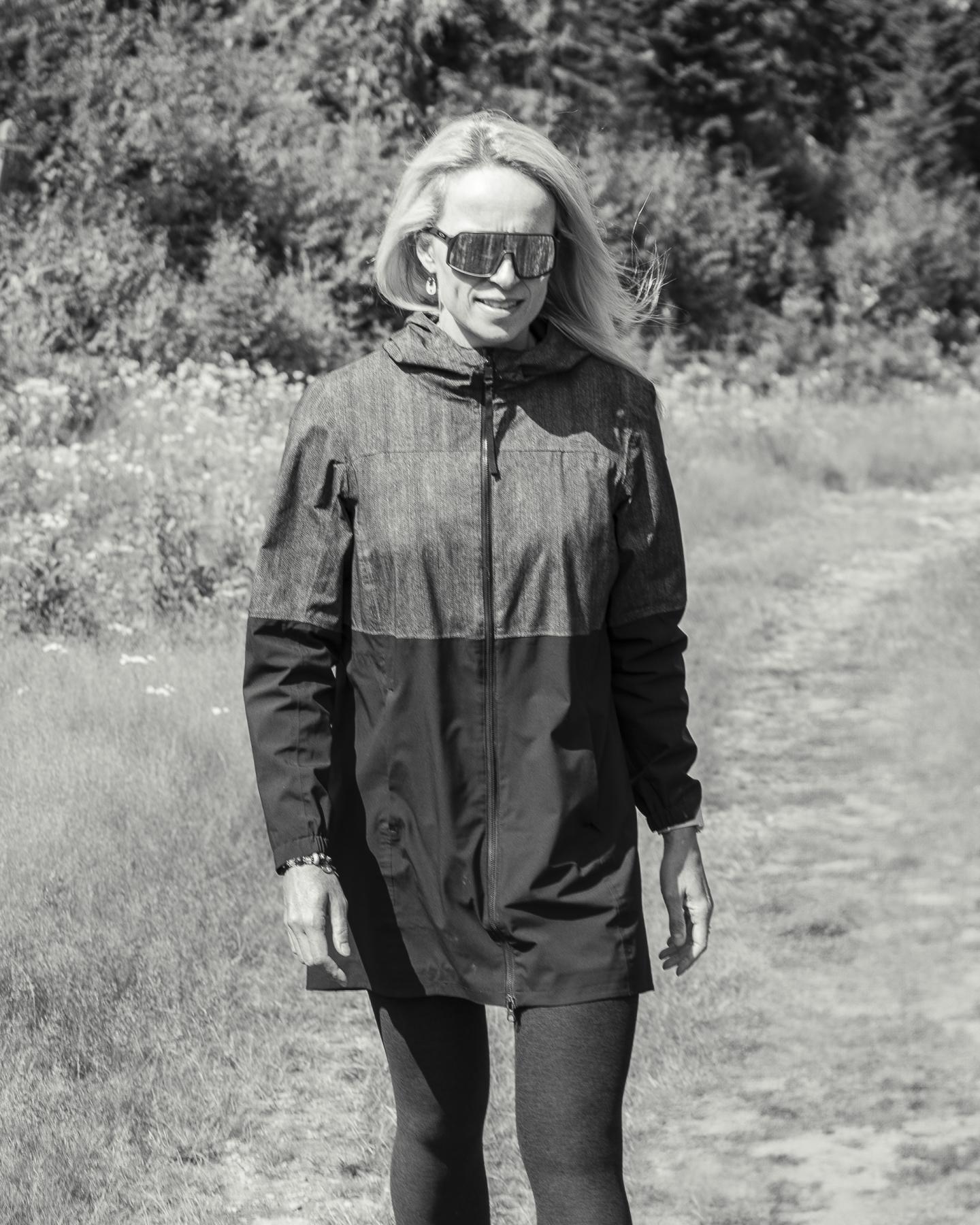 Femme en manteau marchant dans un chemin, forêt en arrière-plan. Photo en noir et blanc.