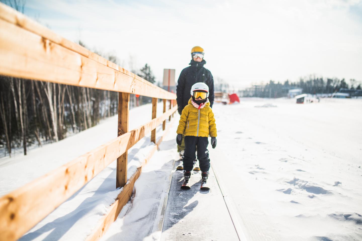 Enfant et adulte en ski sur une piste enneigée, vêtus de manteaux et casques.