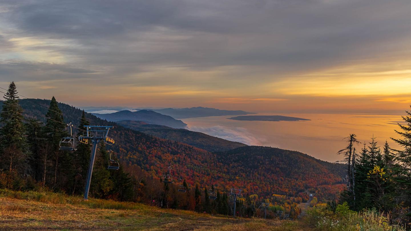 Paysage montagneux au coucher du soleil avec forêt aux couleurs d'automne et télésiège.