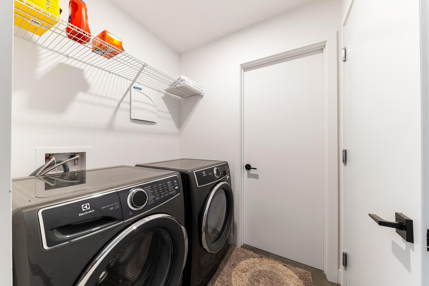 Salle de lavage avec machine à laver et sèche-linge noirs, étagères murales avec produits.