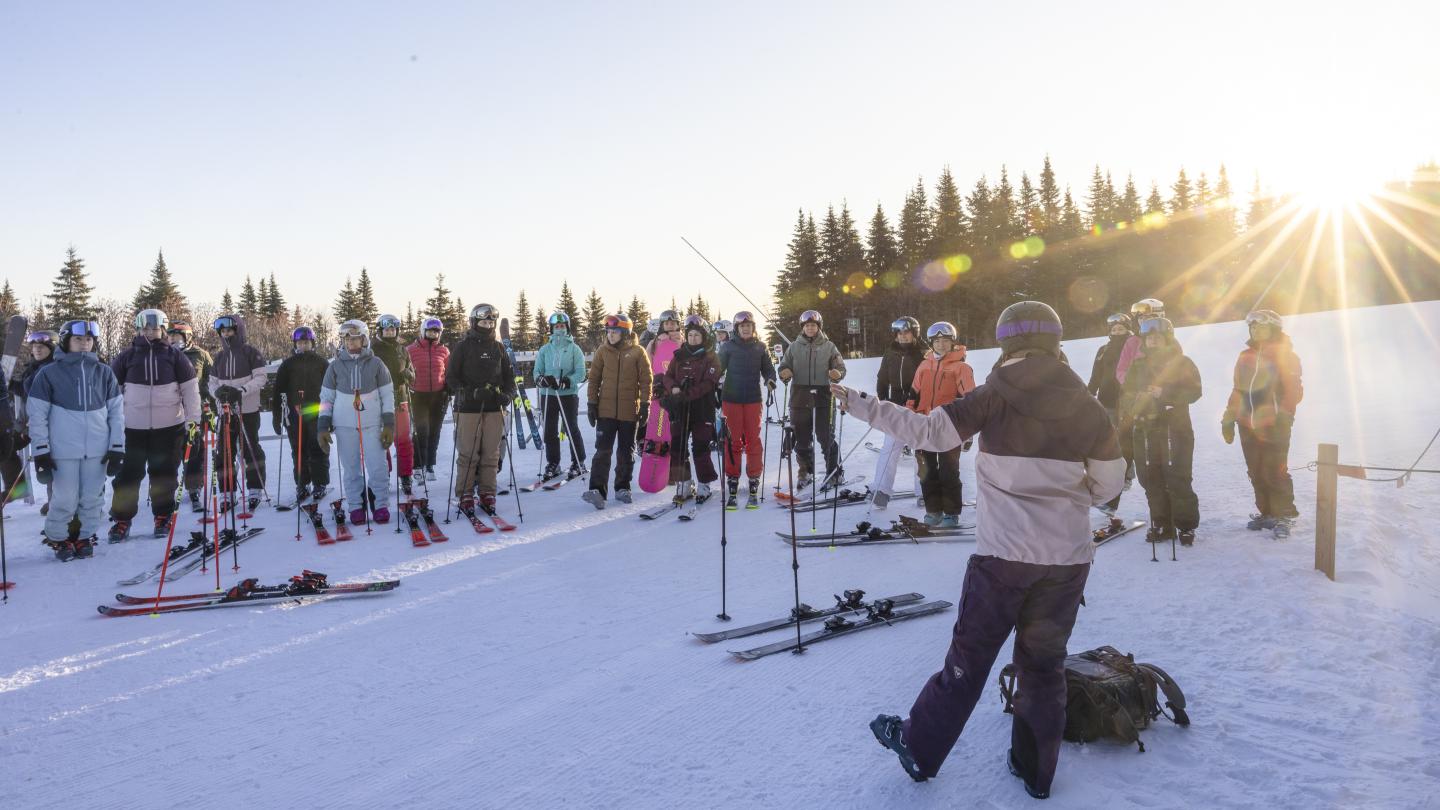 Groupe skieurs écoutant instructeur sur piste enneigée au lever du soleil.