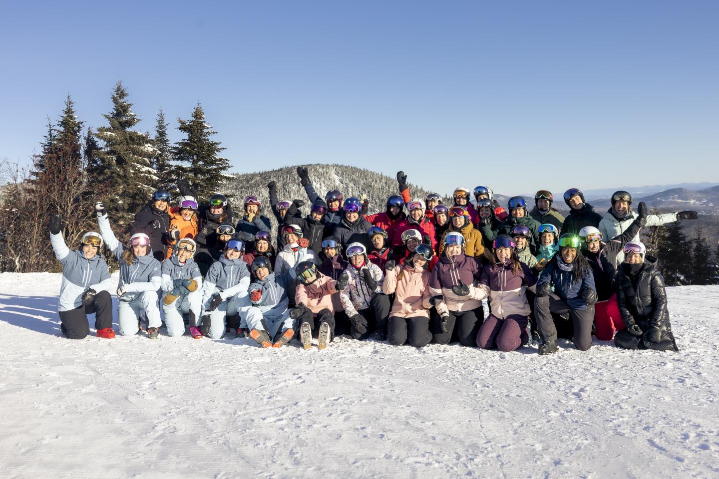 Un groupe de personnes souriantes pose sur une montagne enneigée sous un ciel bleu.