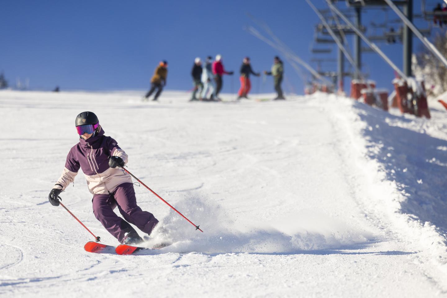 Skieur descendant une piste enneigée par temps ensoleillé accompagné d'un groupe