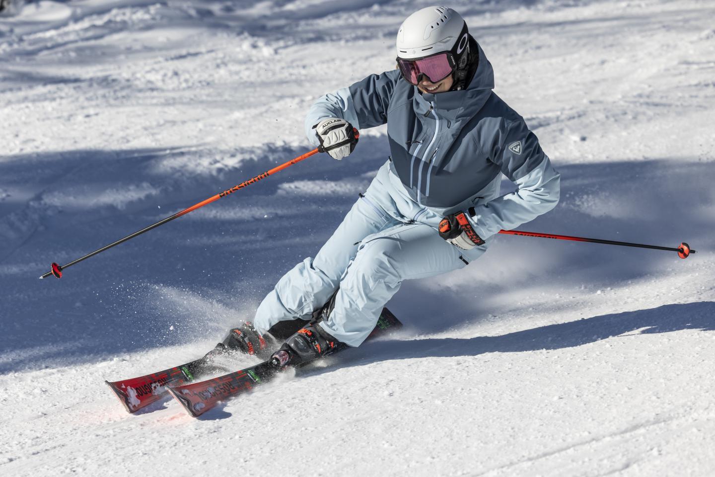 Skieur en combinaison bleue descend une pente enneigée en plein soleil.