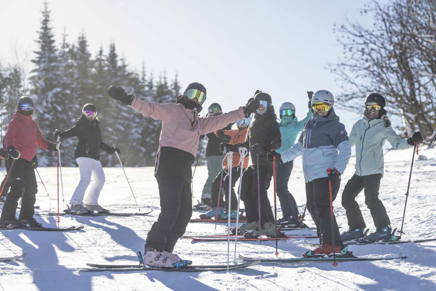 Groupe de skieurs souriants posant sur une piste enneigée ensoleillée.