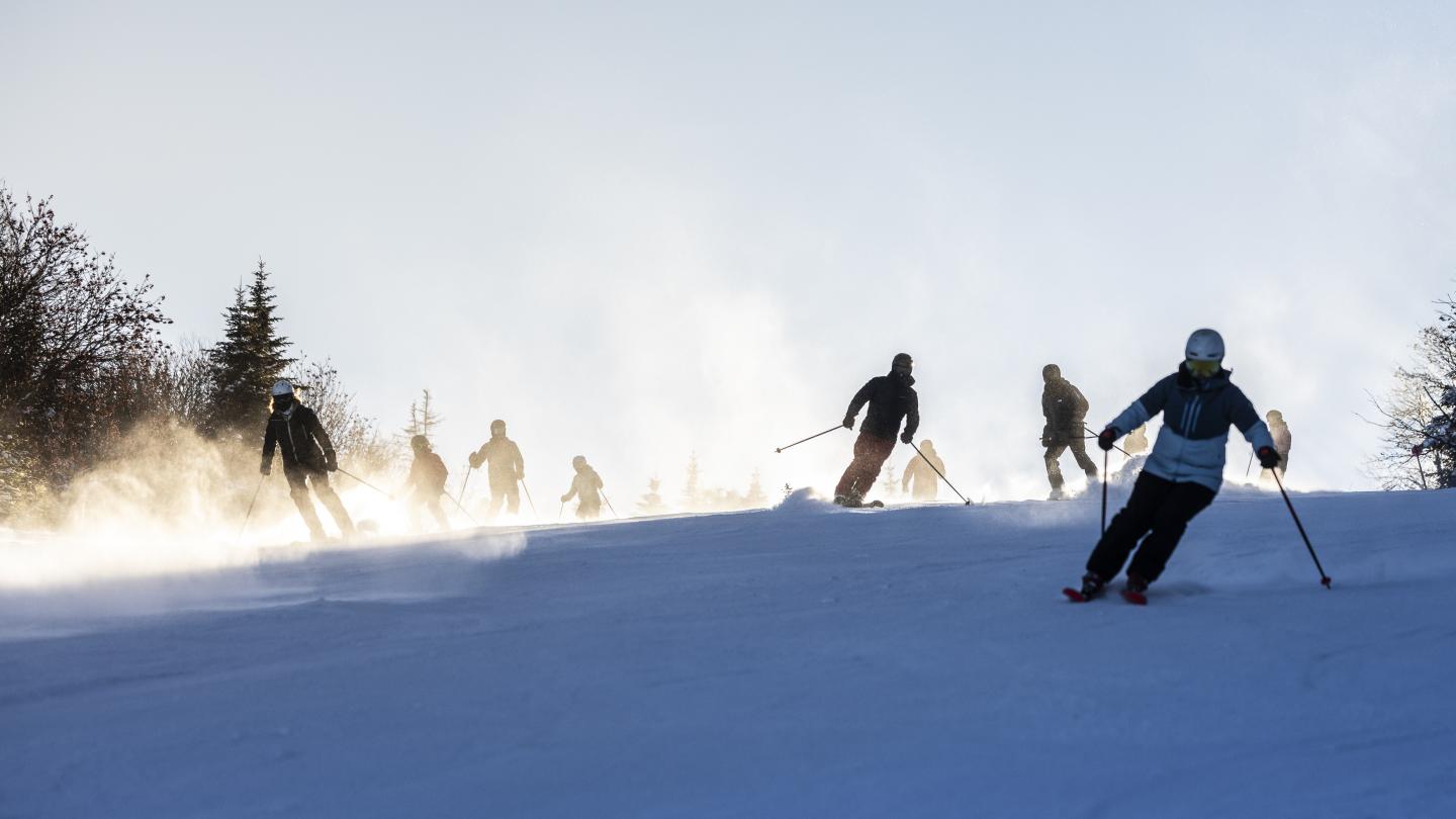 Skiers dévalant une piste enneigée par temps ensoleillé.