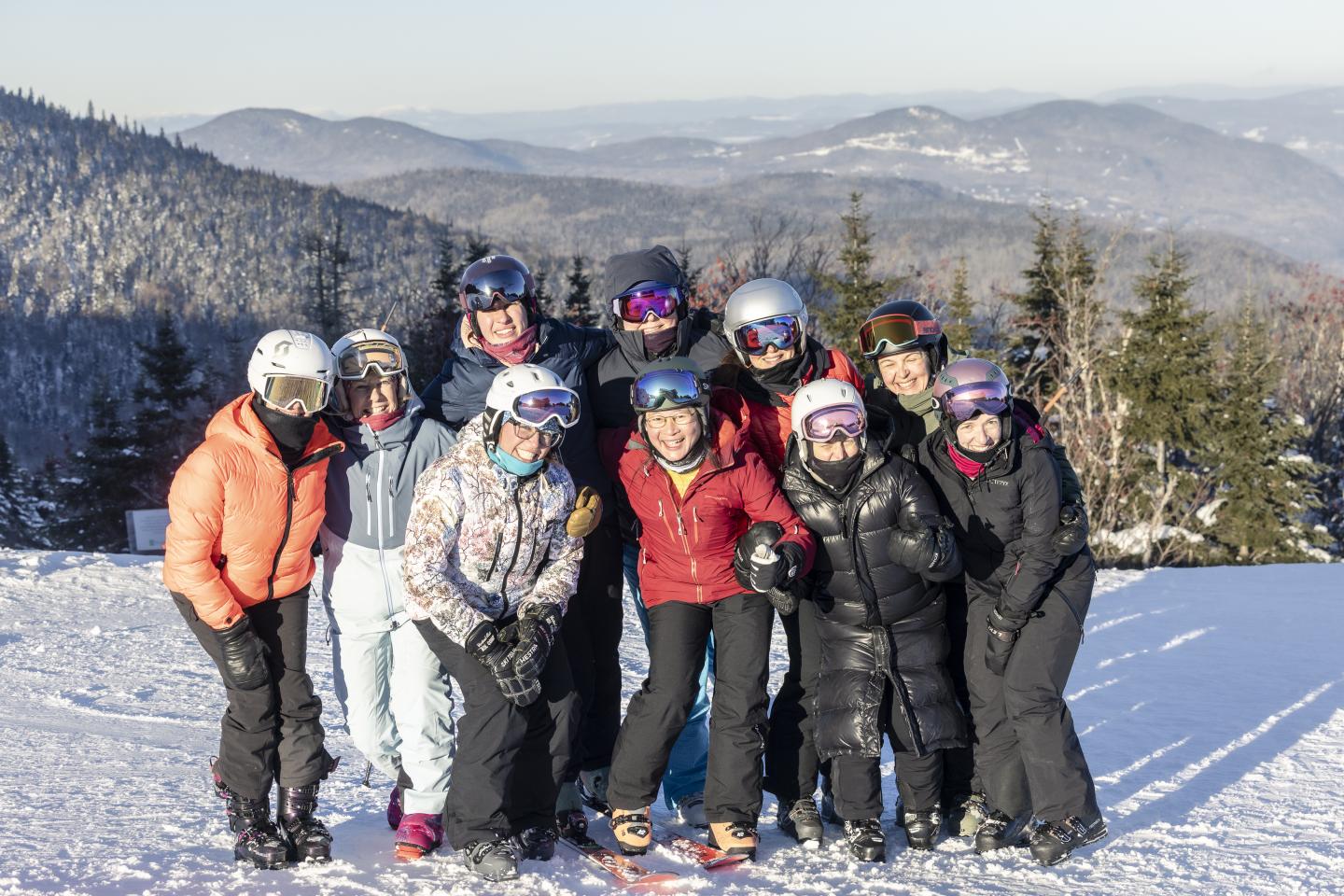 Groupe de personnes en tenue de ski souriant sur une piste enneigée, montagnes en arrière-plan.