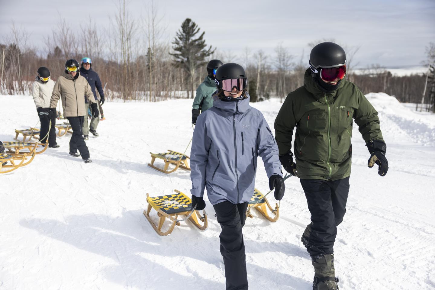 Personnes en veste d'hiver et casque marchant avec des luges sur la neige.