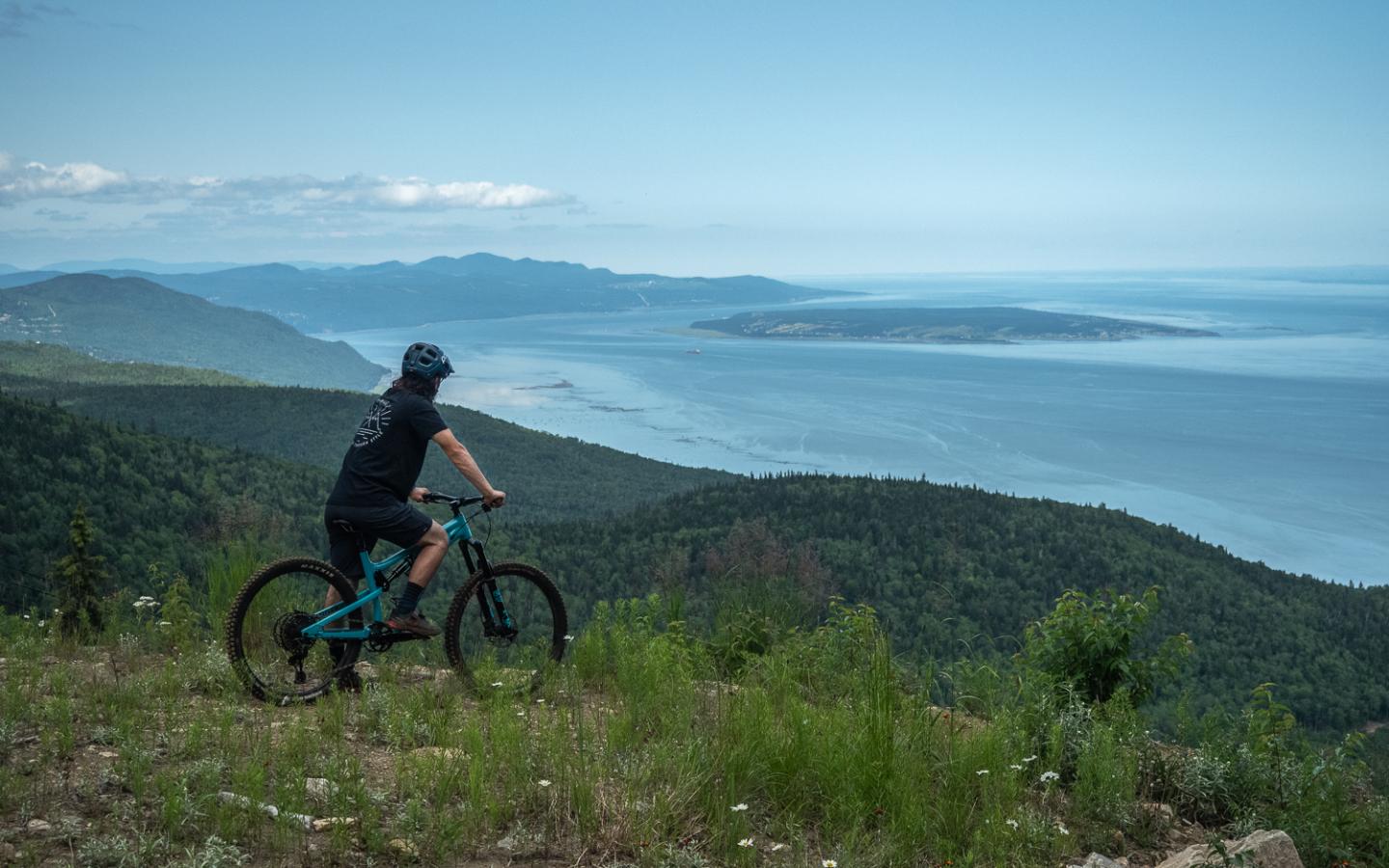 Cycliste sur une colline, vue sur l'océan et les montagnes au loin.