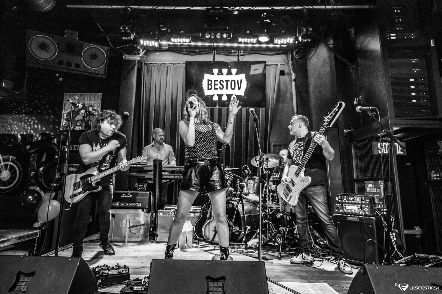 Groupe de rock en concert sur scène, chanteuse au centre. Photo en noir et blanc.