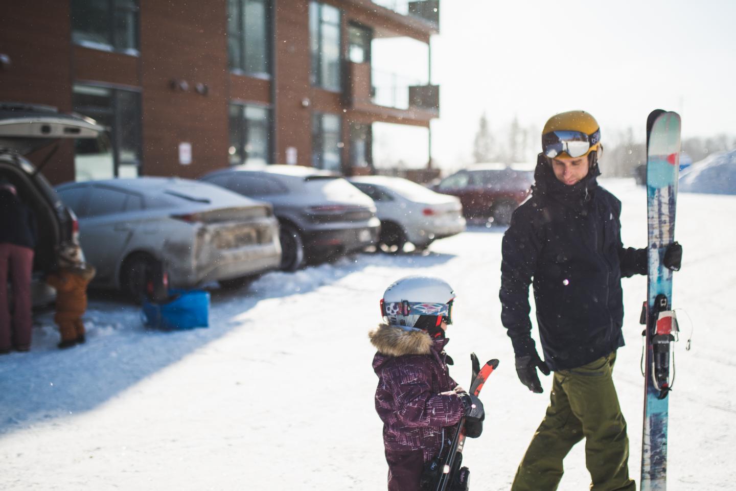 Adulte et enfant en tenue de ski devant un immeuble enneigé.