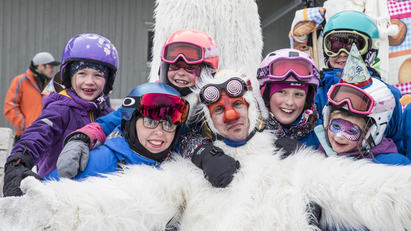 Groupe d'enfants en équipement de ski, souriant avec un homme déguisé en yéti.