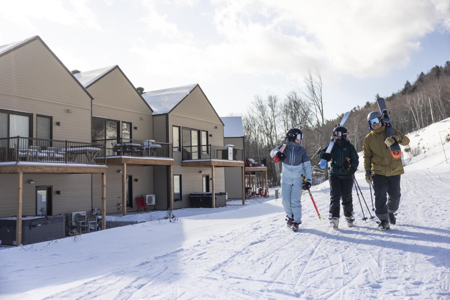 Trois skieurs marchant près de chalets enneigés.