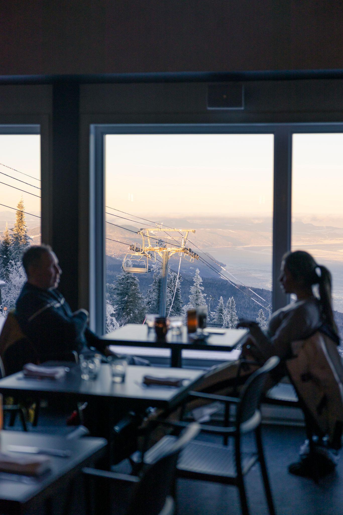 Personnes dînant dans un restaurant avec vue sur la montagne enneigée au coucher du soleil.