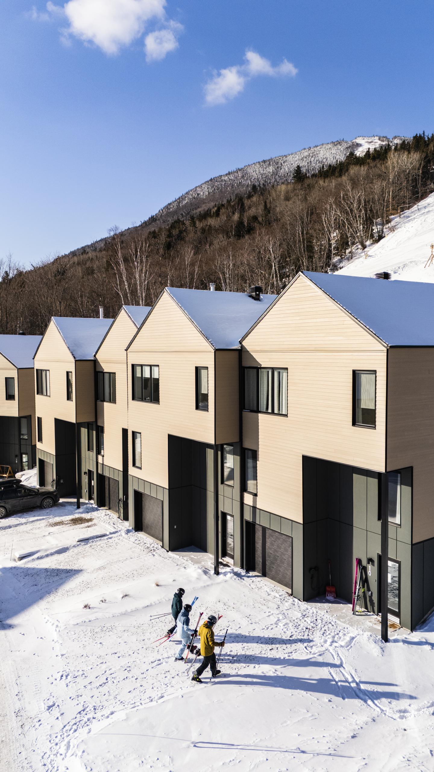 Maisons modernes en hiver, montagne enneigée en arrière-plan, ciel bleu.