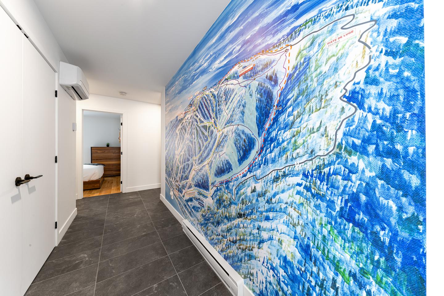 Couloir avec mur décoré d'une fresque abstraite colorée. Salle de bain visible au fond.