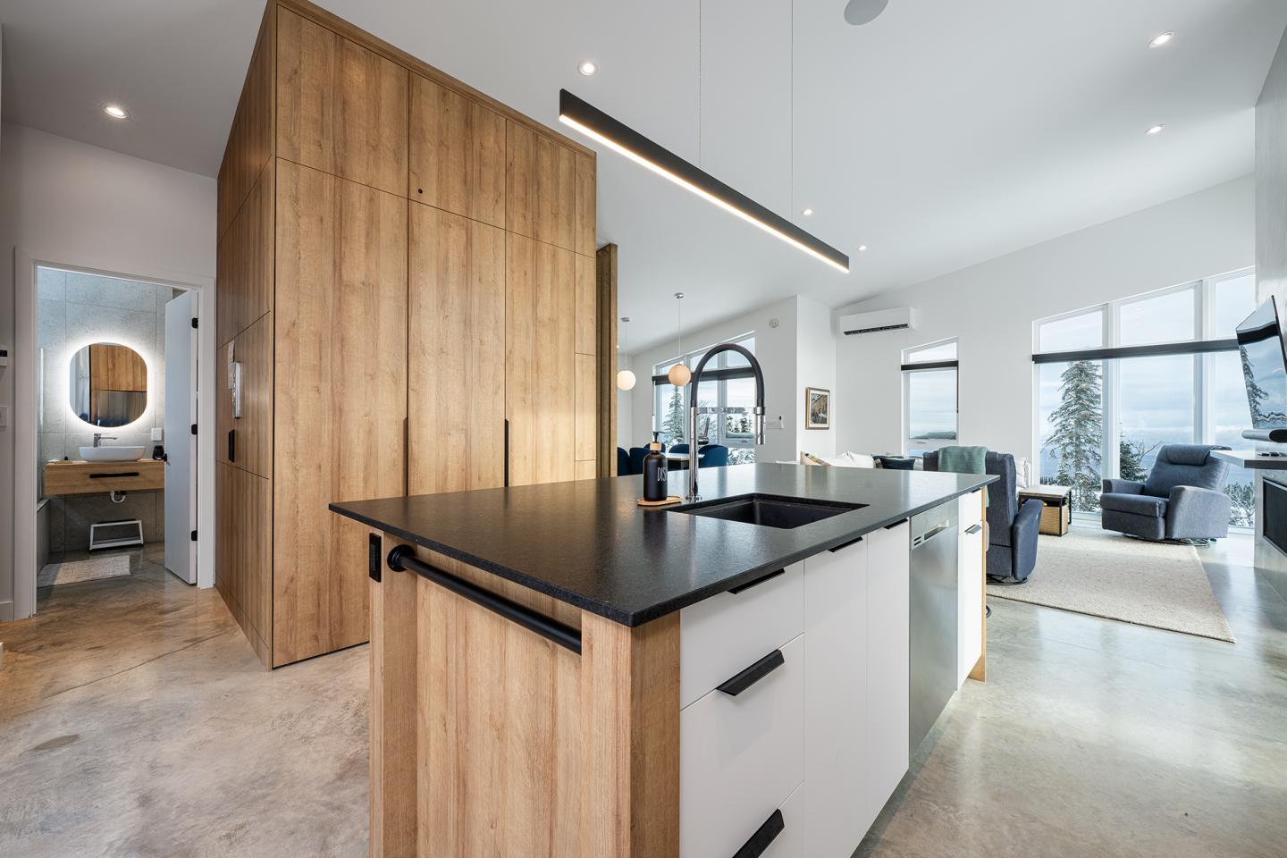 Cuisine moderne, bois clair et plans de travail noirs, ouverte sur le salon lumineux.