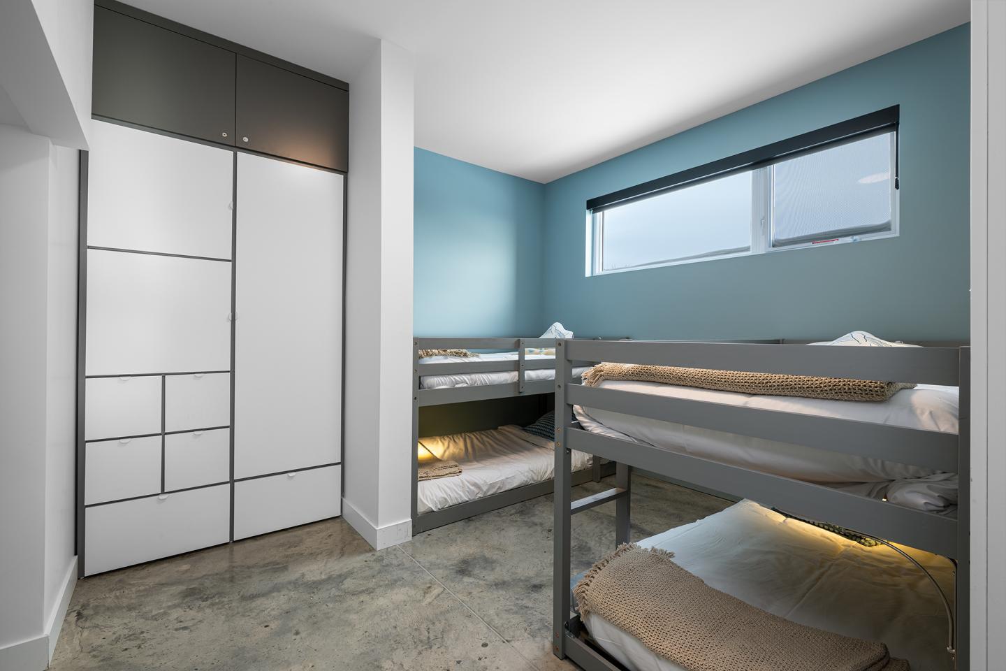 Chambre avec lits superposés, mur bleu, placard blanc et fenêtre.