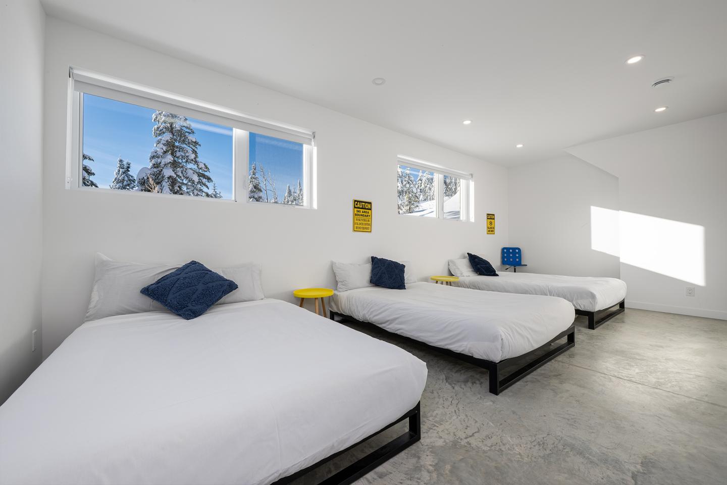 Trois lits avec coussins bleus dans une chambre lumineuse, fenêtres sur un paysage enneigé.