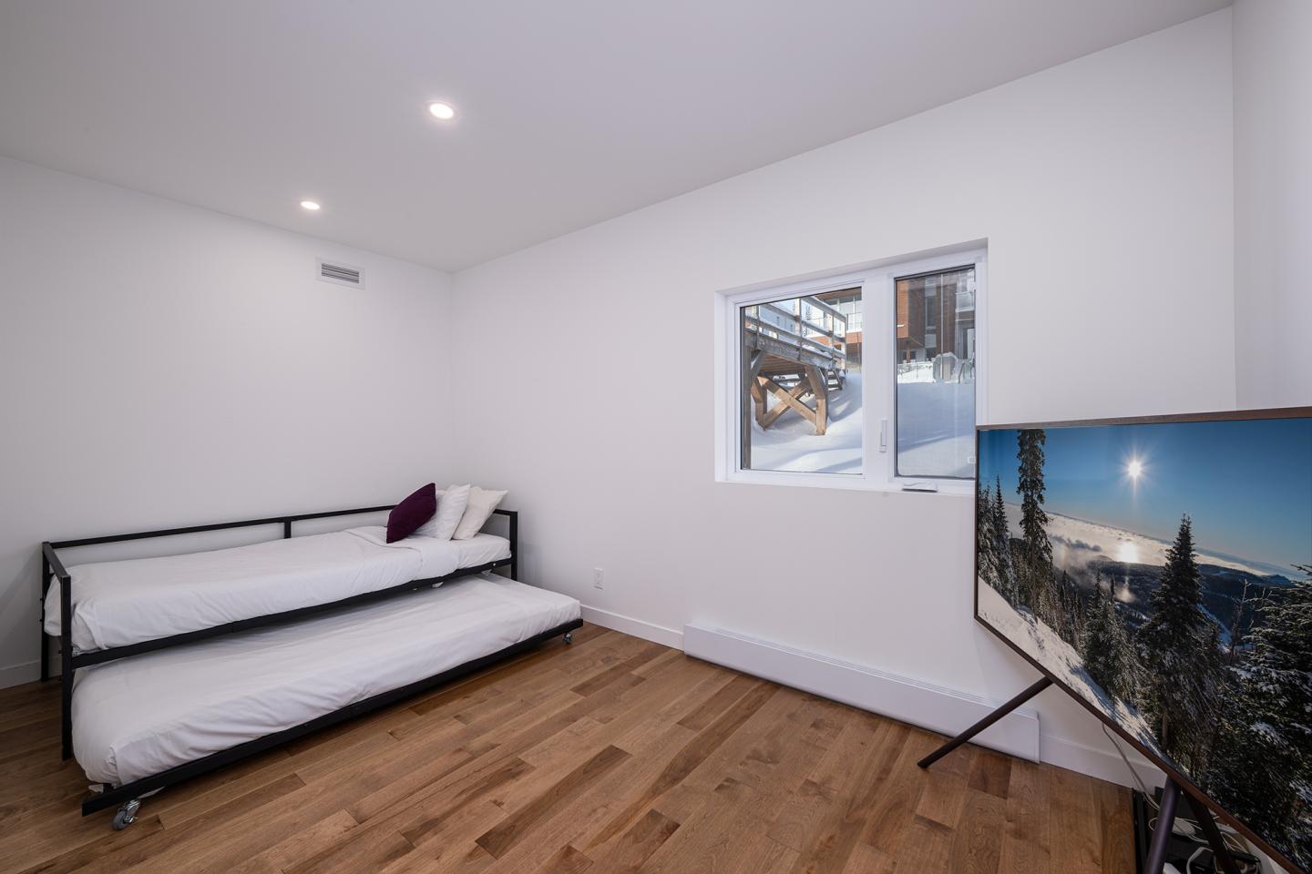 Chambre minimaliste avec lit gigogne et écran affichant un paysage enneigé.