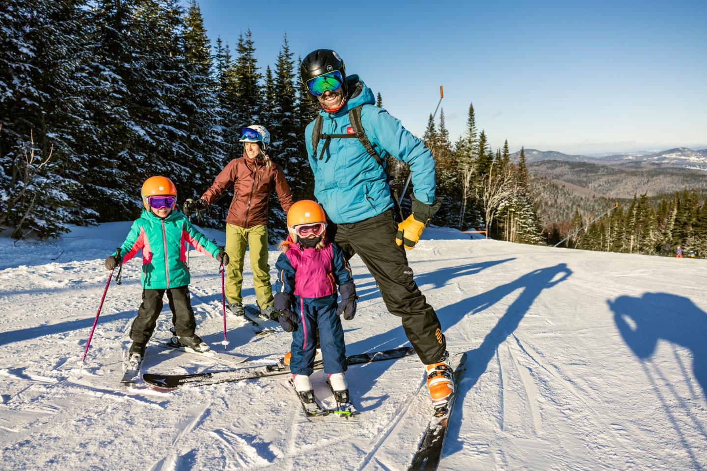 Famille souriante en ski sur une piste enneigée sous un ciel bleu.