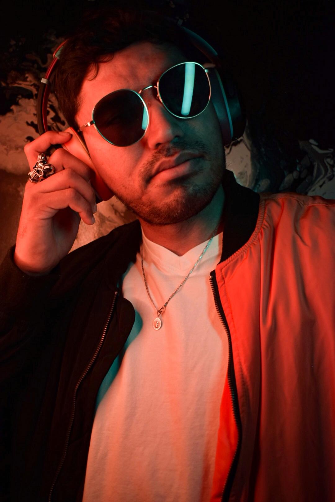 Homme avec lunettes de soleil et casque, veste rouge et éclairage sombre.