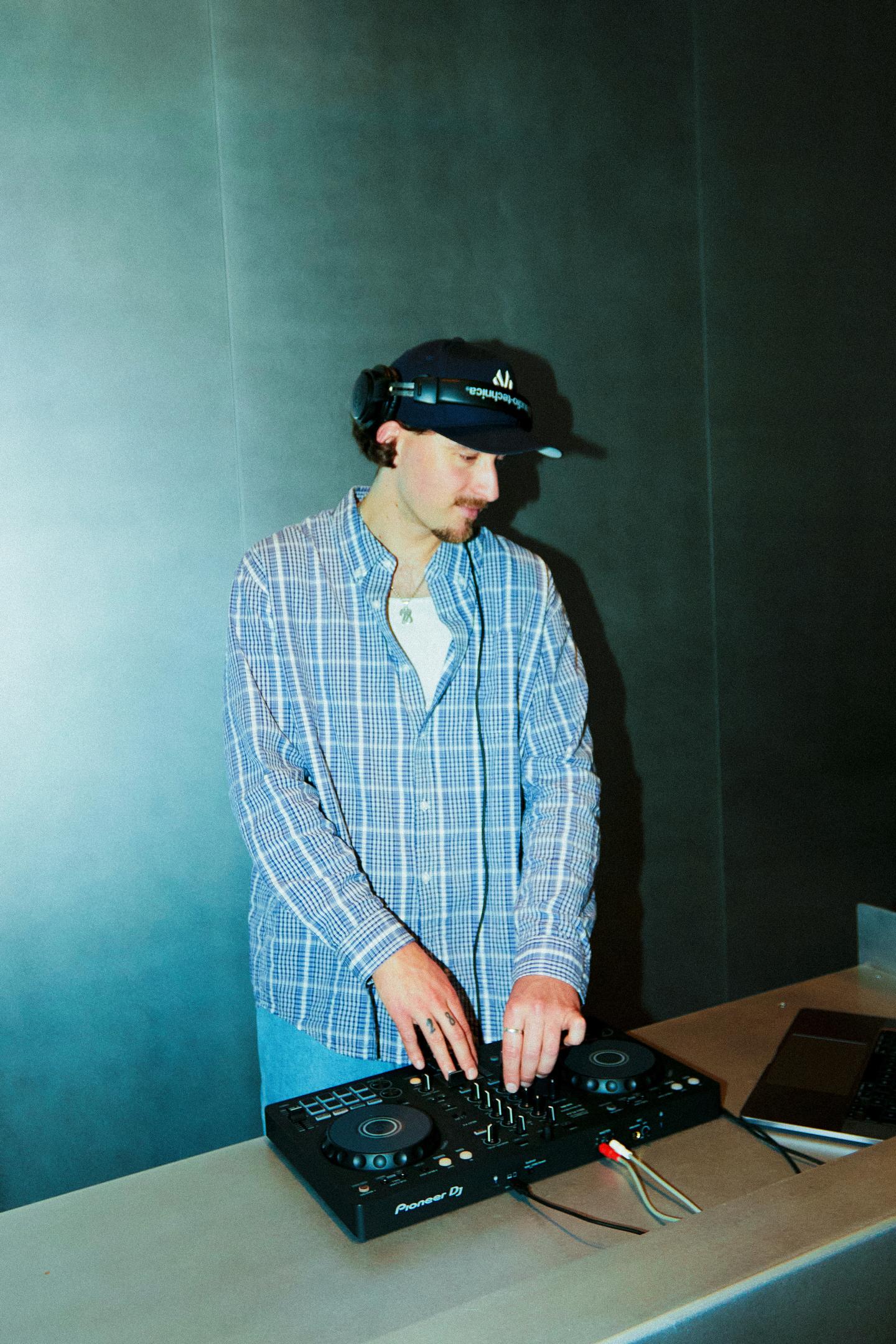 Un DJ avec casquette mixe de la musique sur une table de mix.