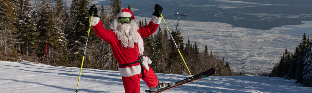Père Noël skiant joyeusement sur une piste enneigée, entouré de sapins.