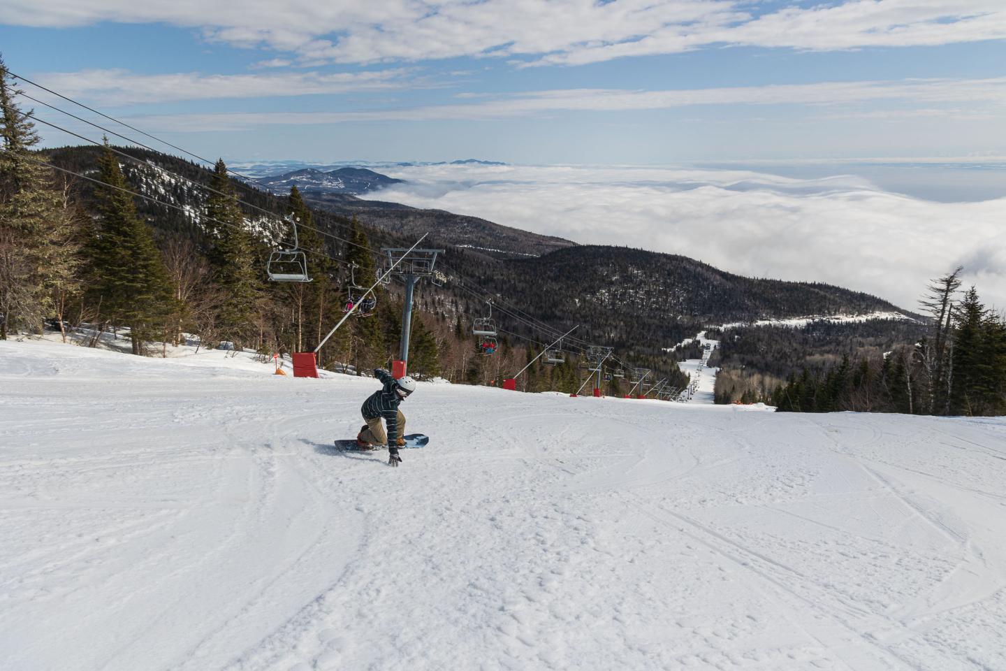 Snowboarder descendant une piste enneigée, montagnes en arrière-plan.