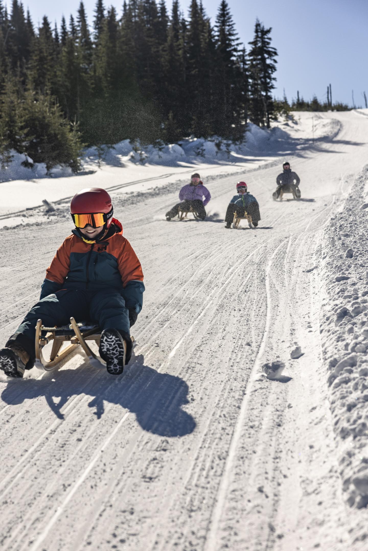 Personnes en luge descendant une piste enneigée sous un ciel ensoleillé.