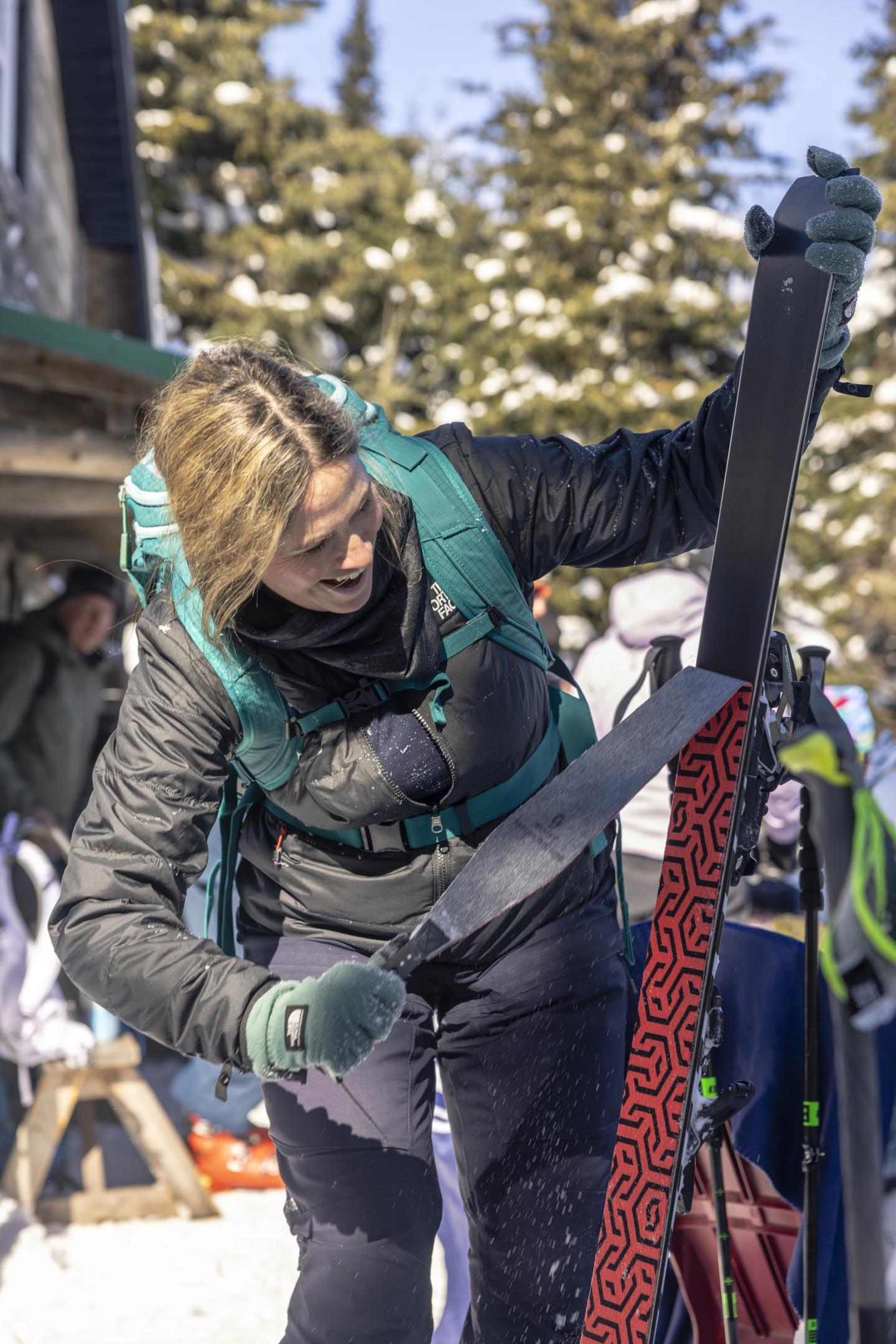 Skieuse préparant ses skis, neige et arbres en arrière-plan.