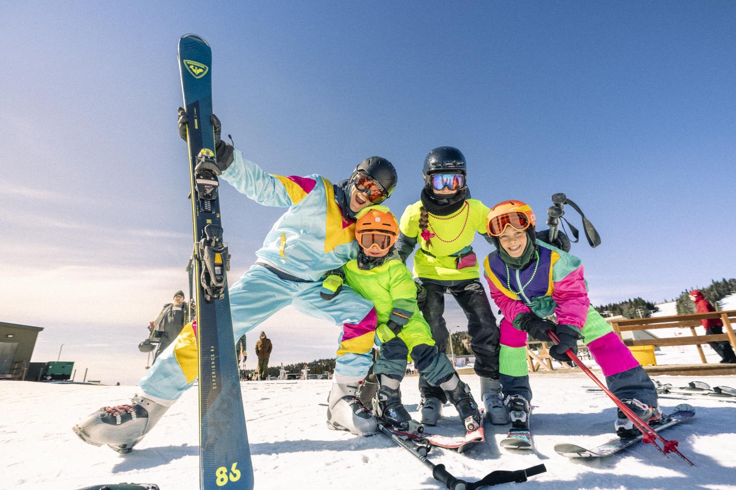 Personnes souriantes en tenues de ski colorées sur une pente enneigée.