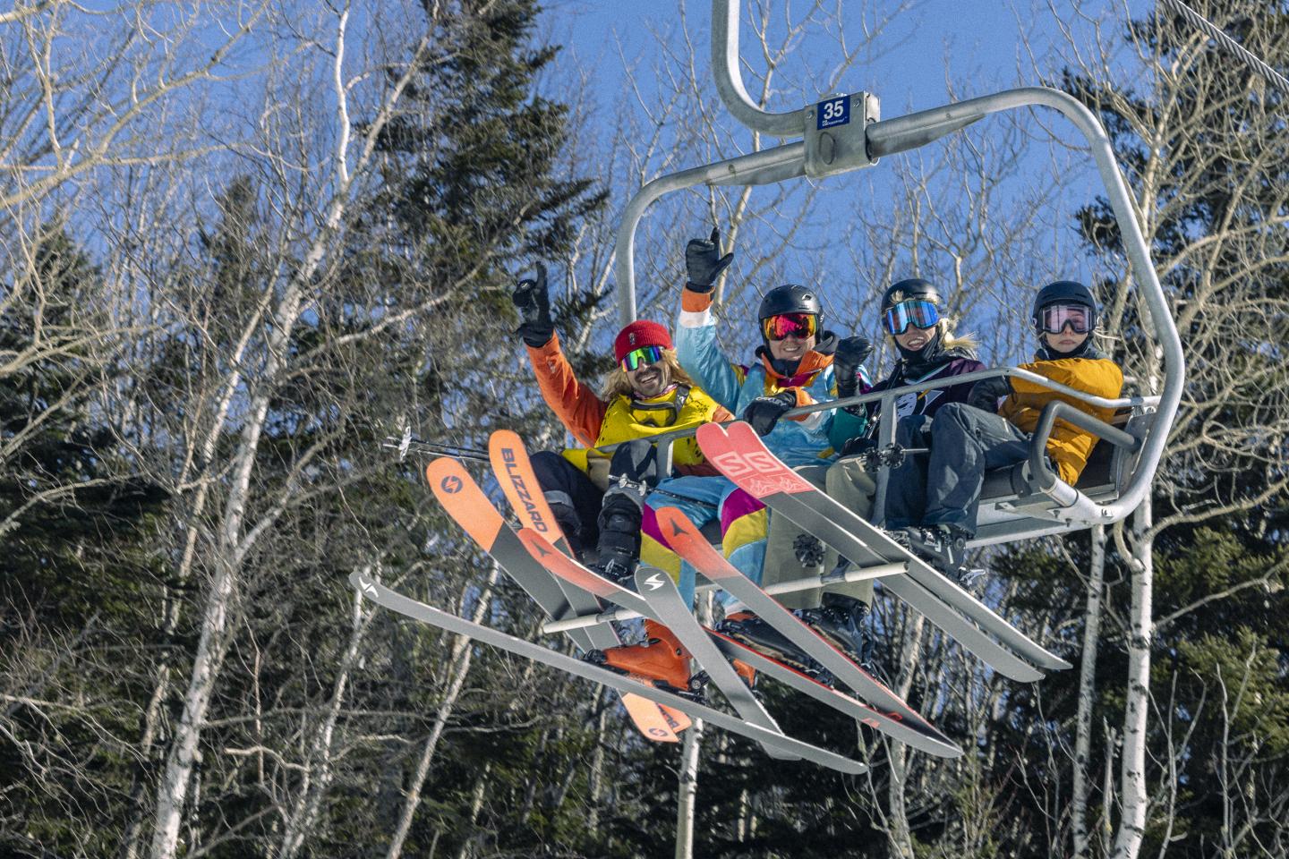 Quatre skieurs souriants sur un télésiège sous un ciel bleu.