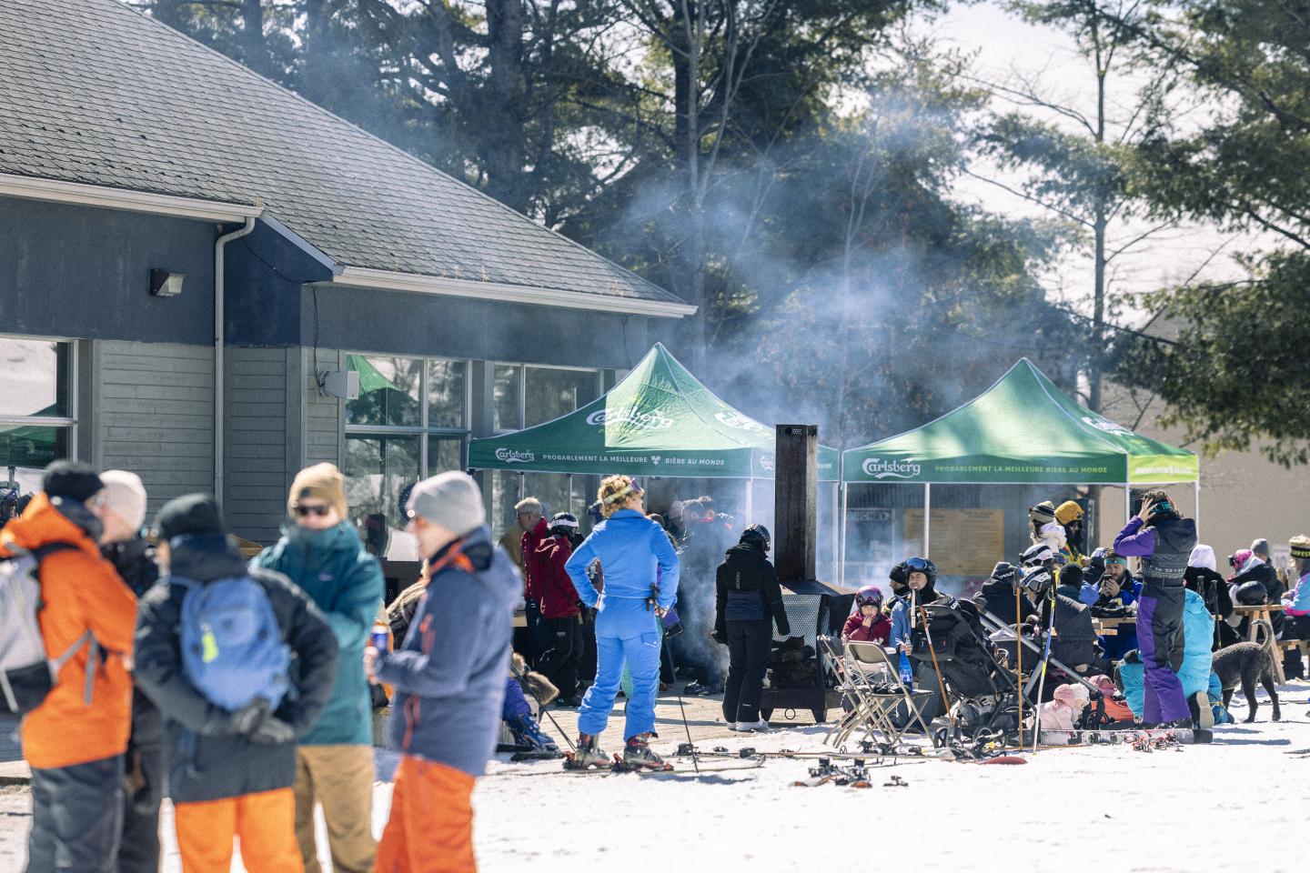 Groupe de skieurs près de tentes vertes et d'un bâtiment, neige au sol.