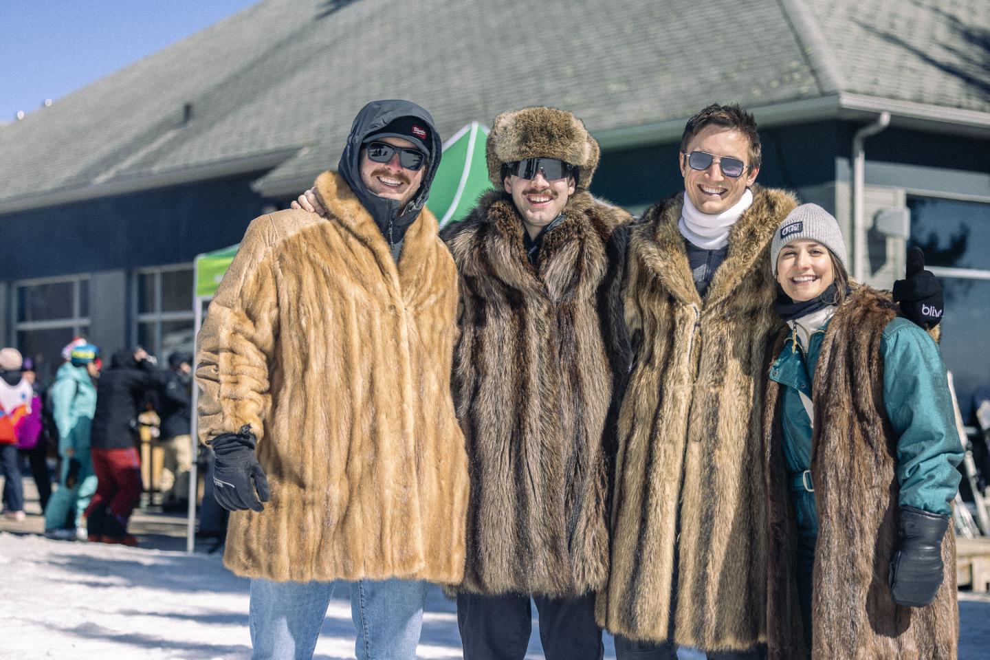 Personnes en manteaux de fourrure posant devant un bâtiment sous la neige.