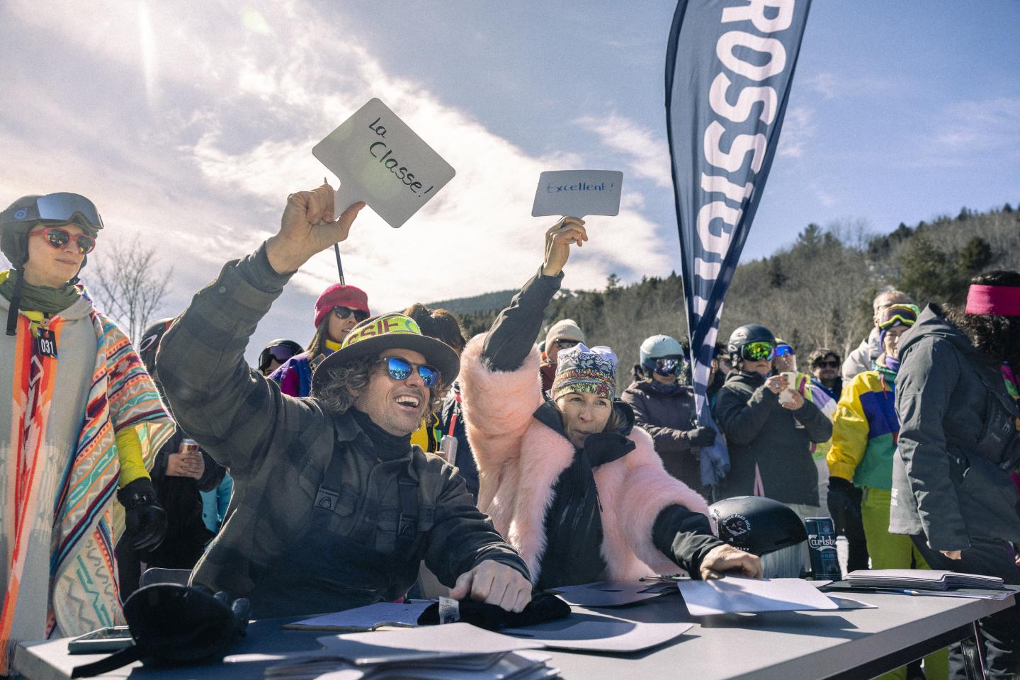 Des juges vêtus de manteaux d'hiver avec des pancartes, en plein air ensoleillé.